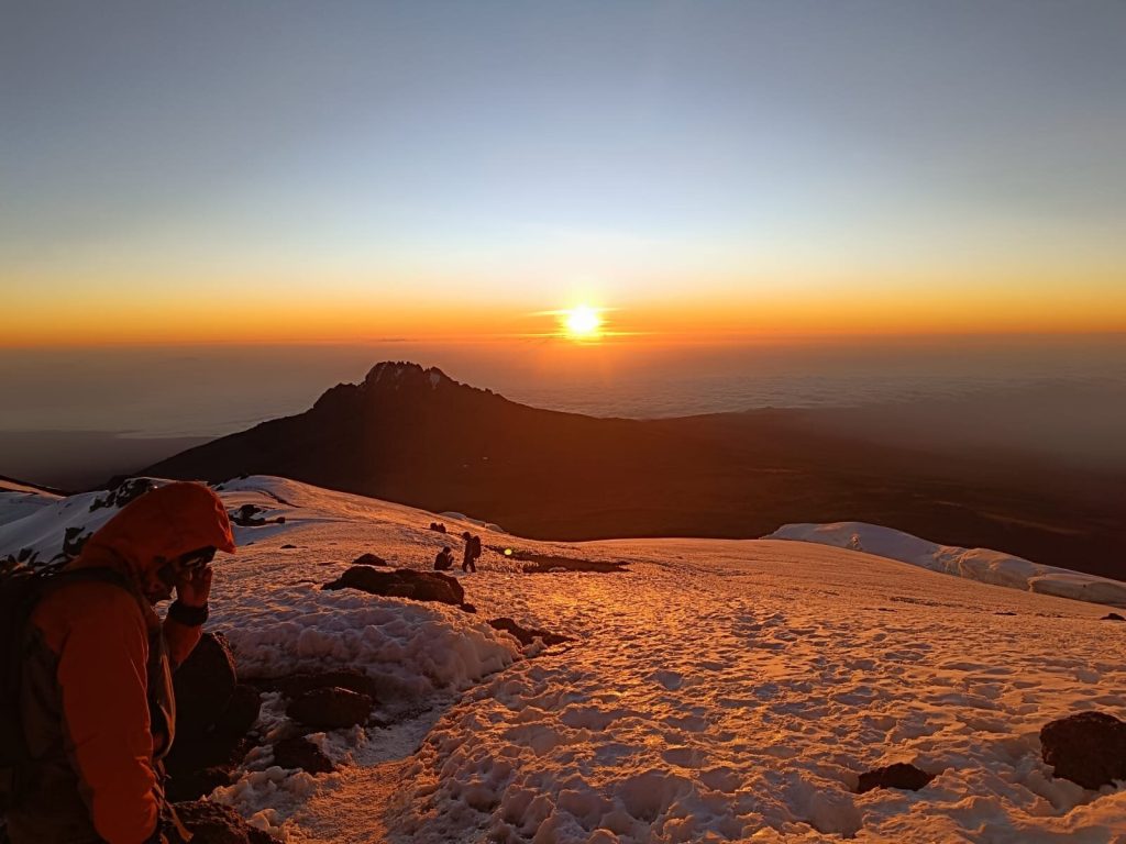Climber in an orange down jacket watching the sunrise near the summit of Kilimanjaro