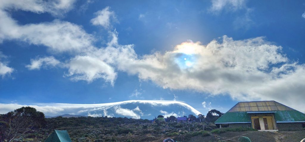 Cloud capped snow dome above moorland camp hut on Mount Kilimanjaro