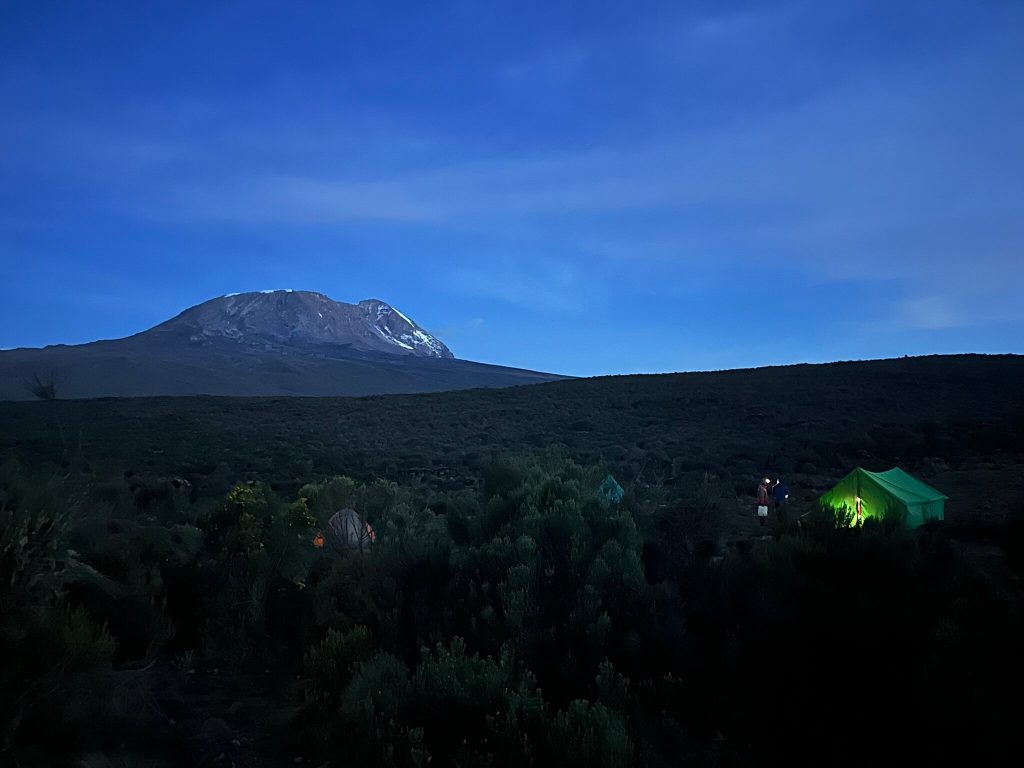 A Kilimanjaro camp at dusk with a glowing green mess tent