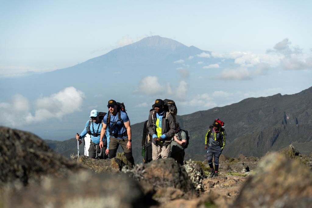 Five trekkers on a rocky ridge below a distant volcanic cone on Mount Kilimanjaro