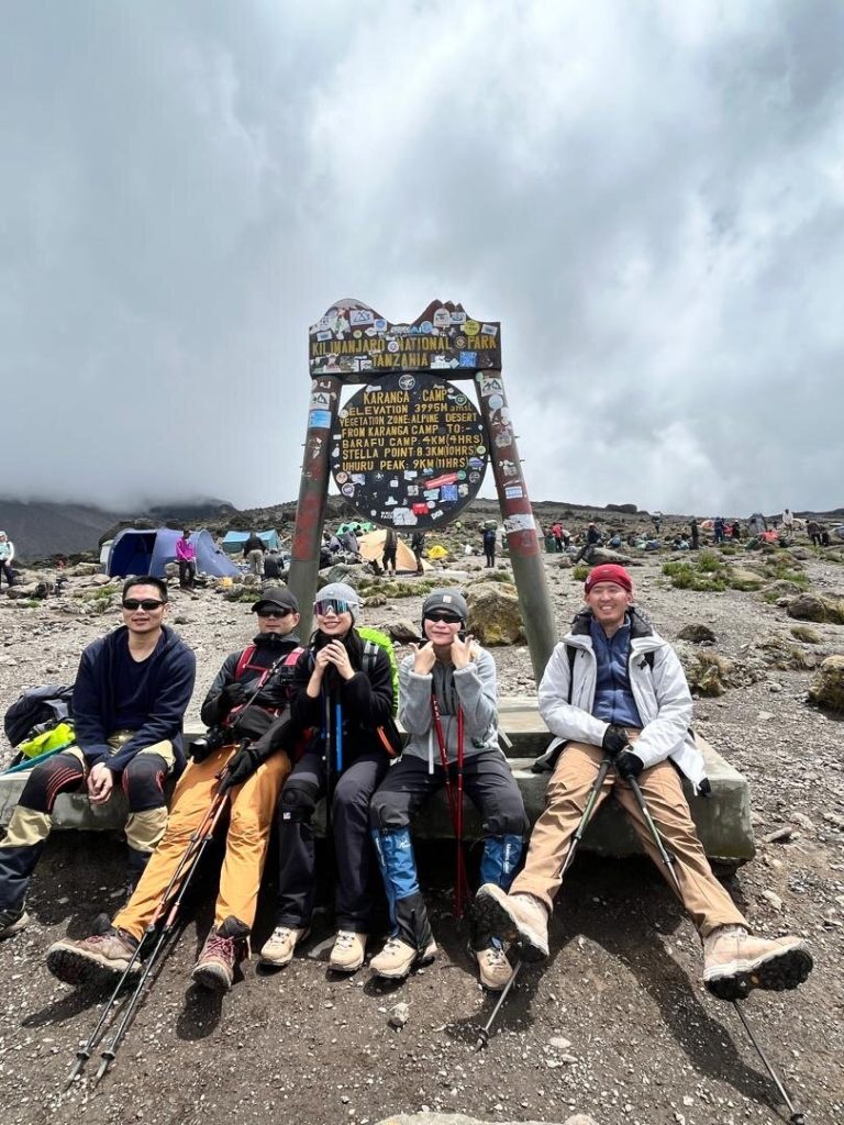 Five trekkers seated at karanga camp signboard on Mount Kilimanjaro