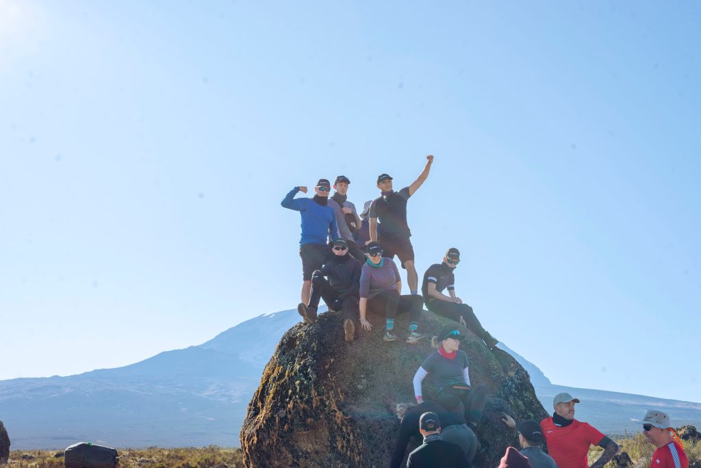 Trekking group posing on a boulder below the snowcapped summit dome of Kilimanjaro