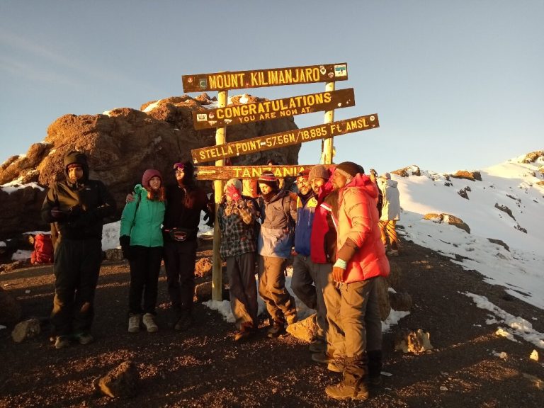 Large group posed at the stella point sign in sunrise light on Mount Kilimanjaro