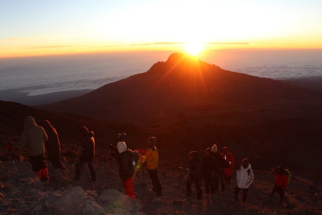A line of trekkers strung out along a rocky slope at sunrise on the Machame Route