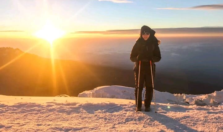 Lone trekker standing on a summit snowfield facing the sunrise on Kilimanjaro