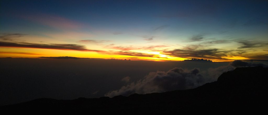 Orange sunset spread across the cloud layer below a high camp on Mount Kilimanjaro