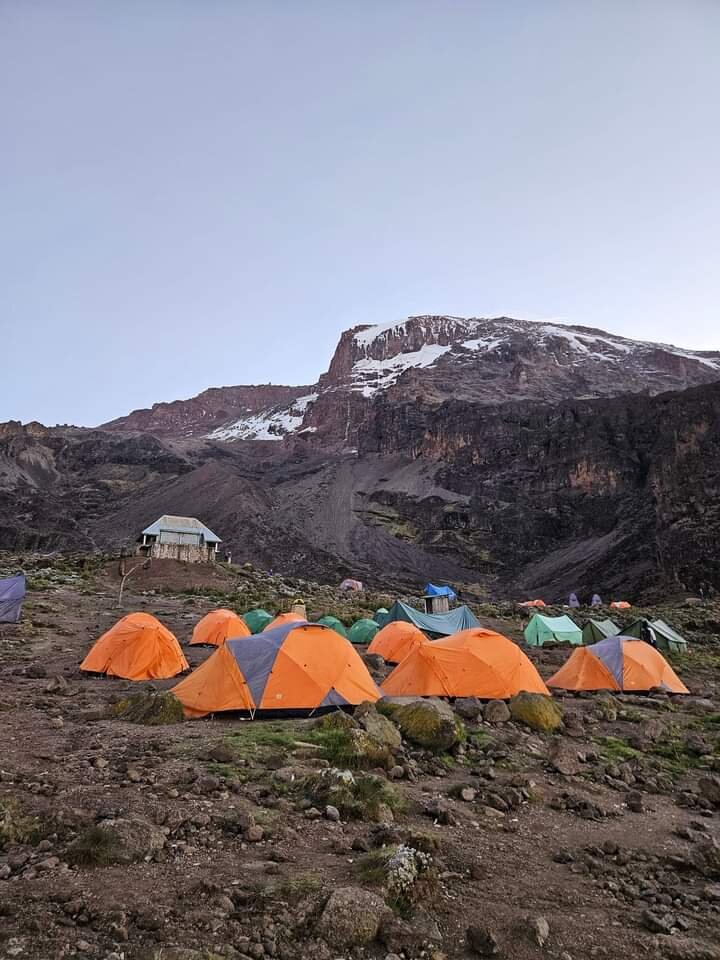 Orange tents at a high camp below a snow-streaked cliff at dusk on Kilimanjaro