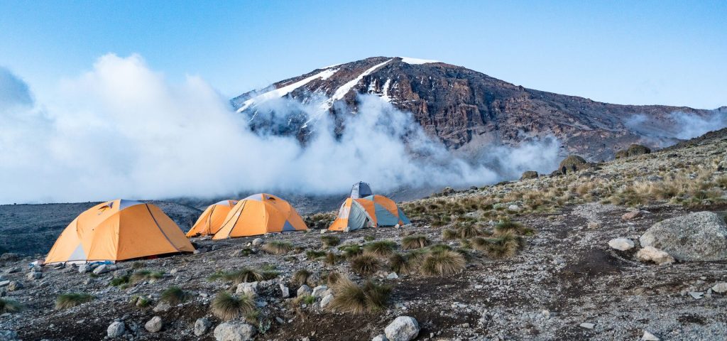 Orange tents below cloud wrapped kibo on Mount Kilimanjaro