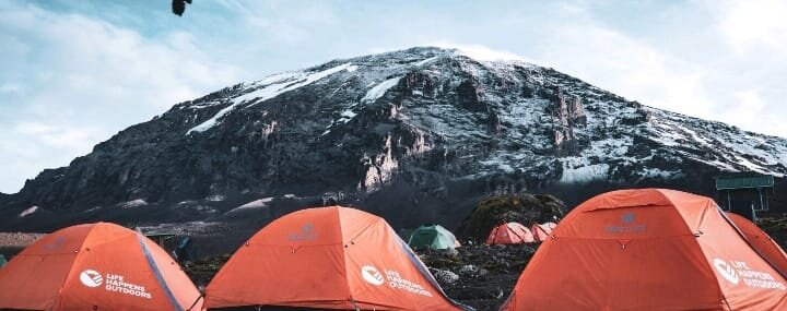 Orange tents below snow streaked summit cone on Mount Kilimanjaro
