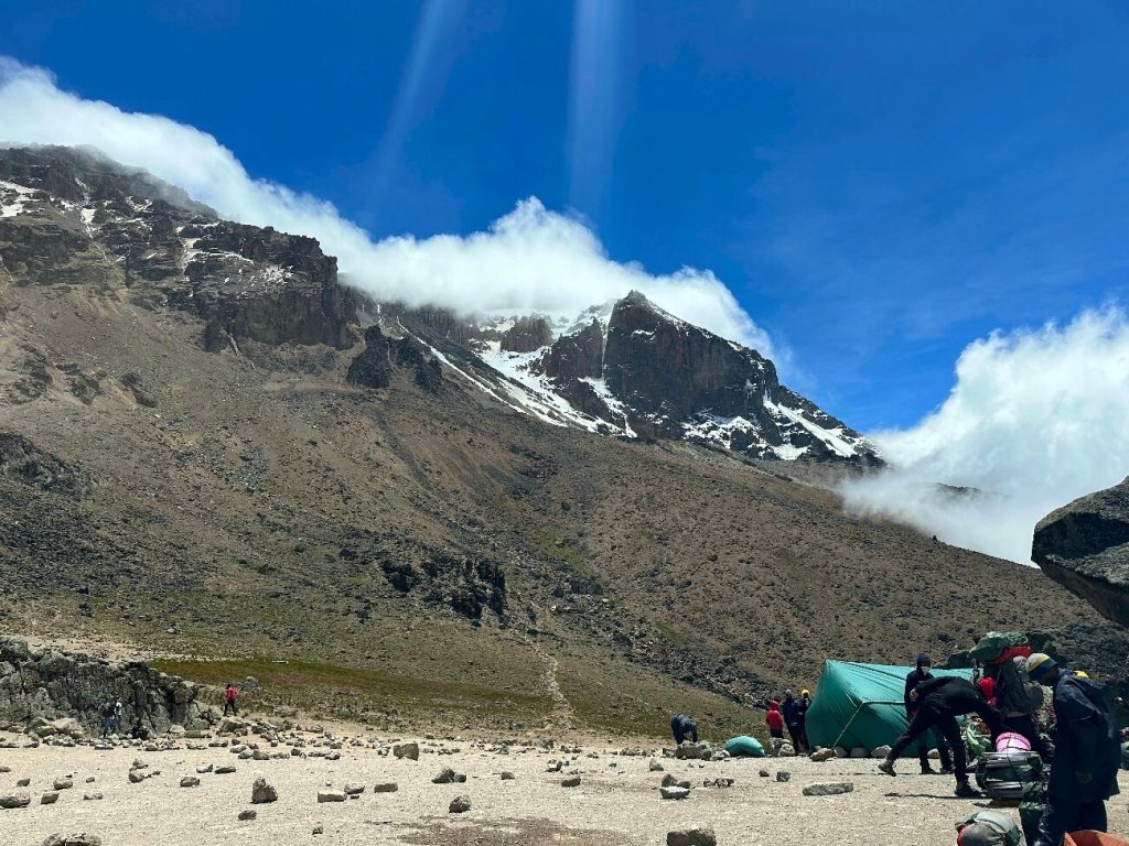 Porters and a green mess tent at Barranco Camp below snow streaked cliffs on Mount Kilimanjaro