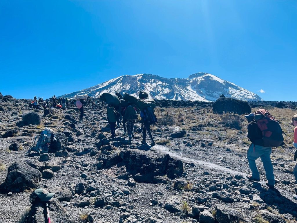 Porters carrying loads toward snow capped kibo on Mount Kilimanjaro