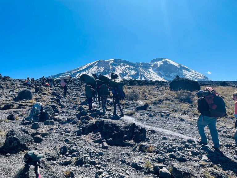 Porters carrying loads toward snow capped kibo on Mount Kilimanjaro