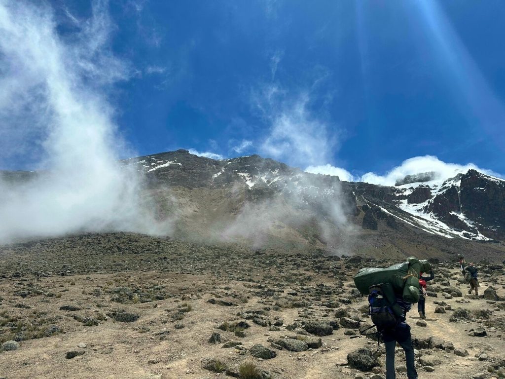 Porters with green loads on dusty alpine desert trail on Mount Kilimanjaro