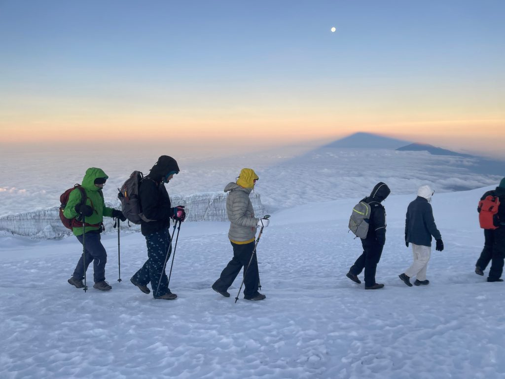 Six trekkers crossing a summit snowfield under moonlight on Kilimanjaro