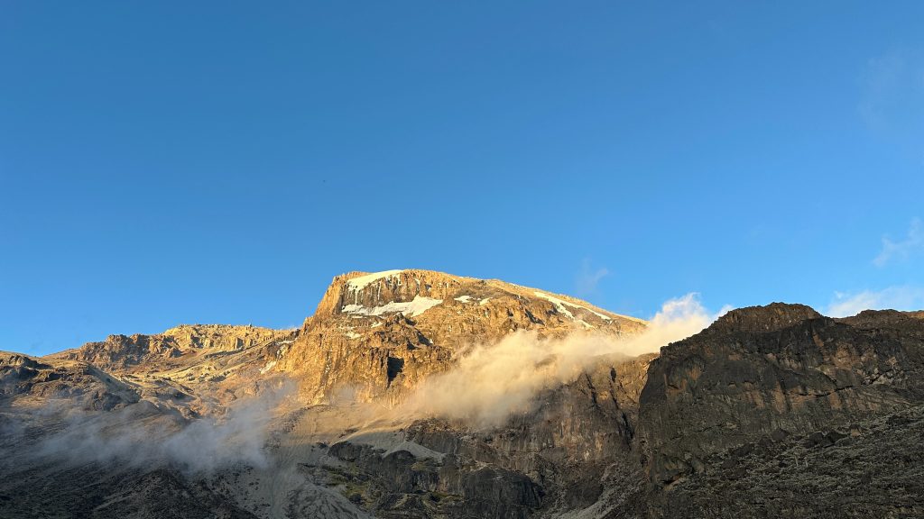 Sunlit rock peak with patches of snow emerging through cloud on Mount Kilimanjaro