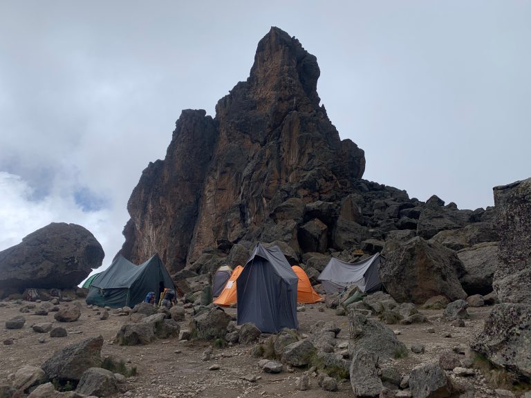 Tents beneath a jagged rock tower in mist on Mount Kilimanjaro