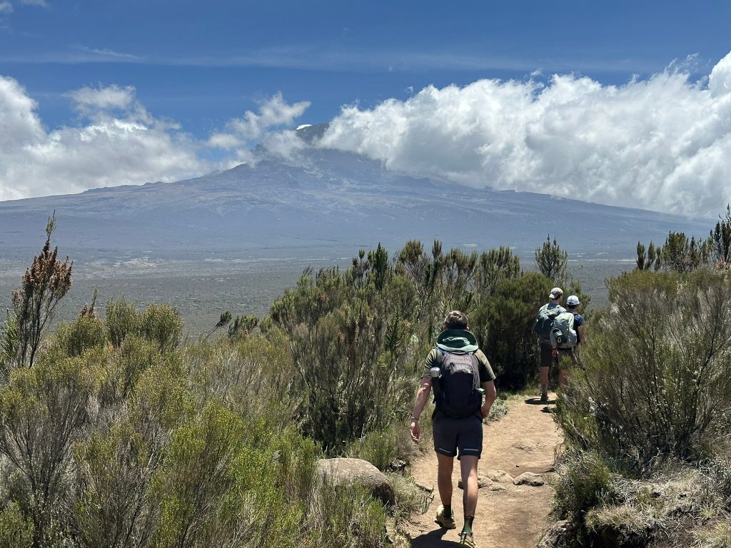 Three trekkers on moorland trail below clouds on Mount Kilimanjaro