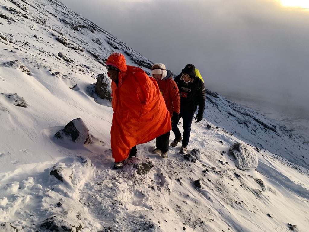 Three trekkers walking down a snowy slope at sunrise on Mount Kilimanjaro