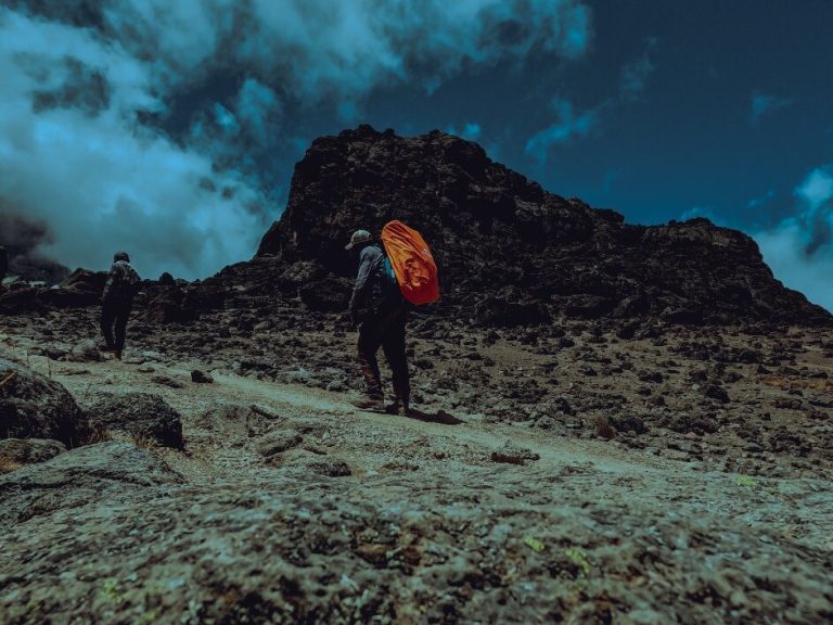 Trekker with orange pack on dark scree on Mount Kilimanjaro