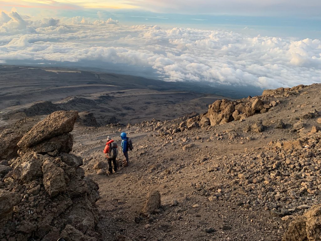 Two trekkers on alpine desert scree above a sea of cloud on Mount Kilimanjaro