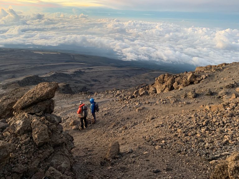 Two trekkers on alpine desert scree above a sea of cloud on Mount Kilimanjaro