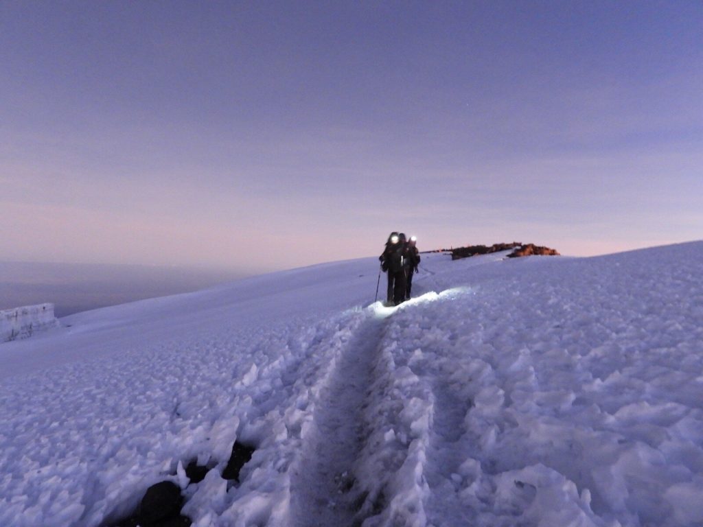 Two trekkers with headlamps on predawn summit snowfield on Mount Kilimanjaro