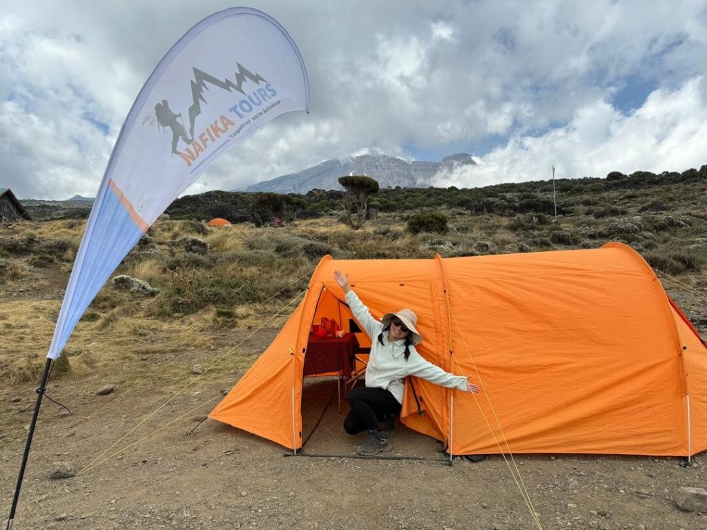 Woman by orange tent with operator banner on Mount Kilimanjaro