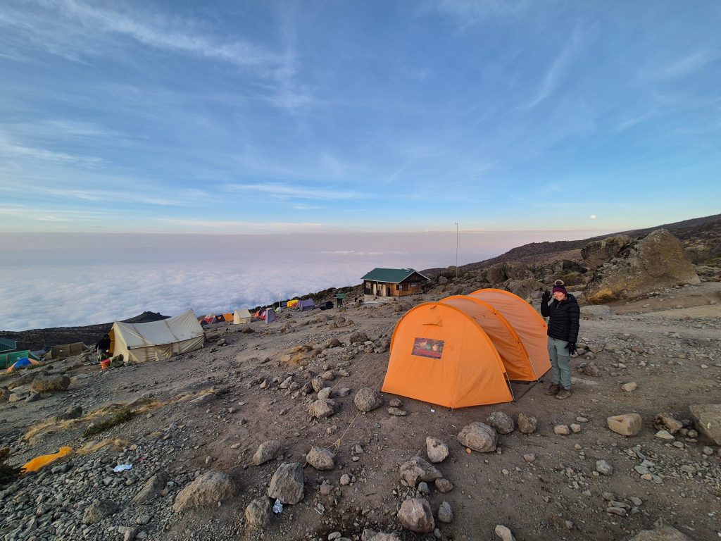 Woman waving by orange tent above clouds on Mount Kilimanjaro